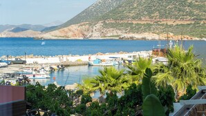 A coastal marina with boats docked, a rocky hillside in the background, and lush greenery in the foreground. - Bali Seaside Sailor (Mylopotamos)