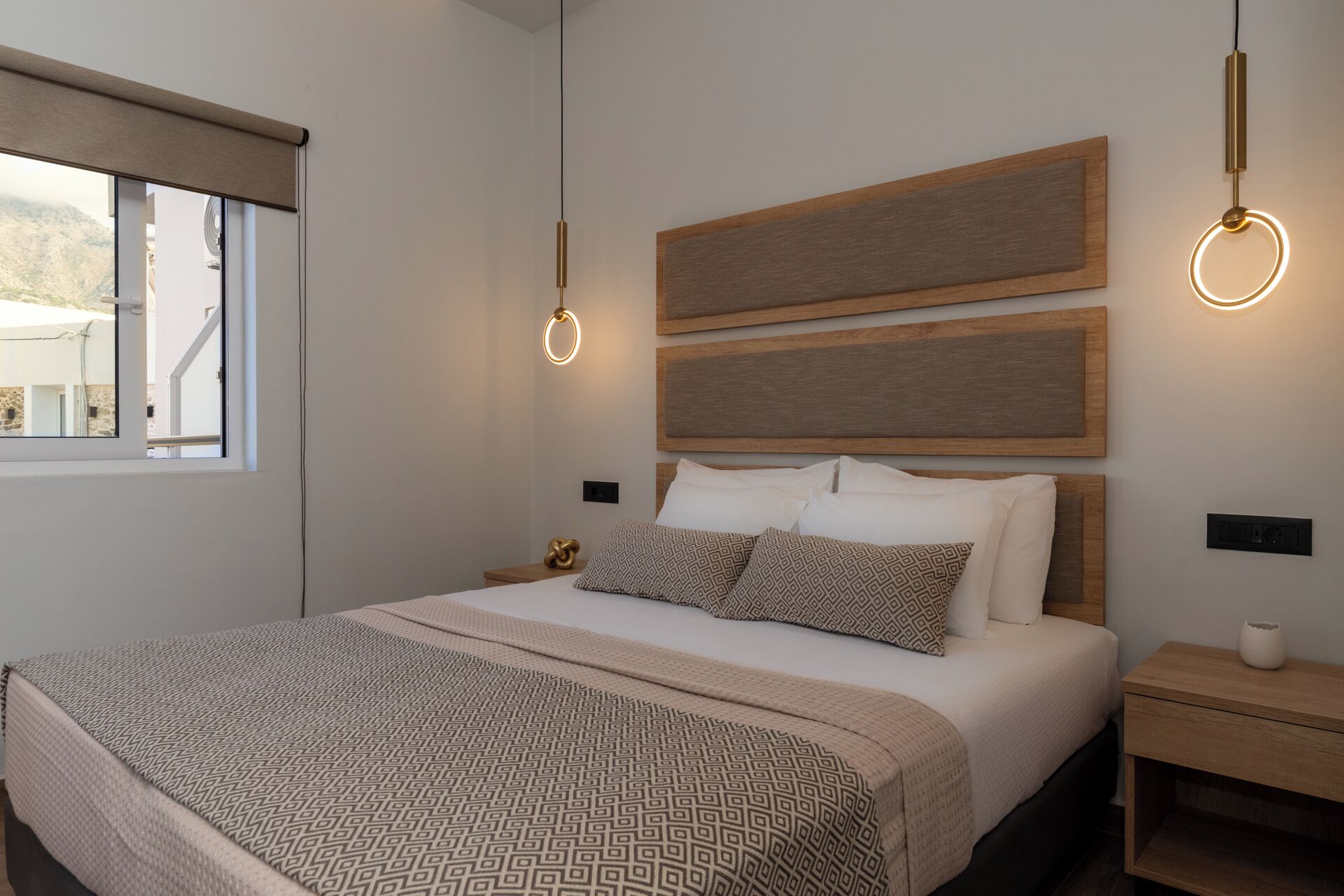 Een moderne slaapkamer met een groot bed, een houten hoofdbord en twee hanglampen.