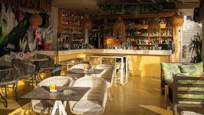 A bar area with wicker furniture, a mural, and shelves stocked with bottles. - Bali Seaside Sailor (Mylopotamos)
