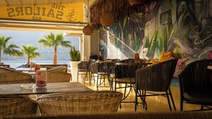 A restaurant with wicker furniture, a mural, and a view of the sea. - Bali Seaside Sailor (Mylopotamos)