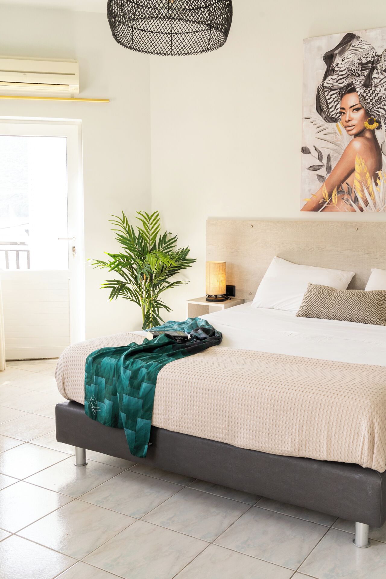 A modern bedroom with a large bed, a potted plant, and a wall-mounted lamp.