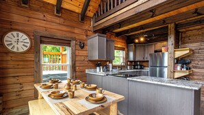 A wooden cabin with a kitchen featuring a wooden table set with bowls and cups, a clock, and a refrigerator.