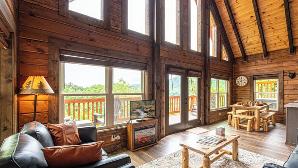 A spacious cabin with a large living area featuring a fireplace, wooden furniture, and large windows offering views of the outdoors.