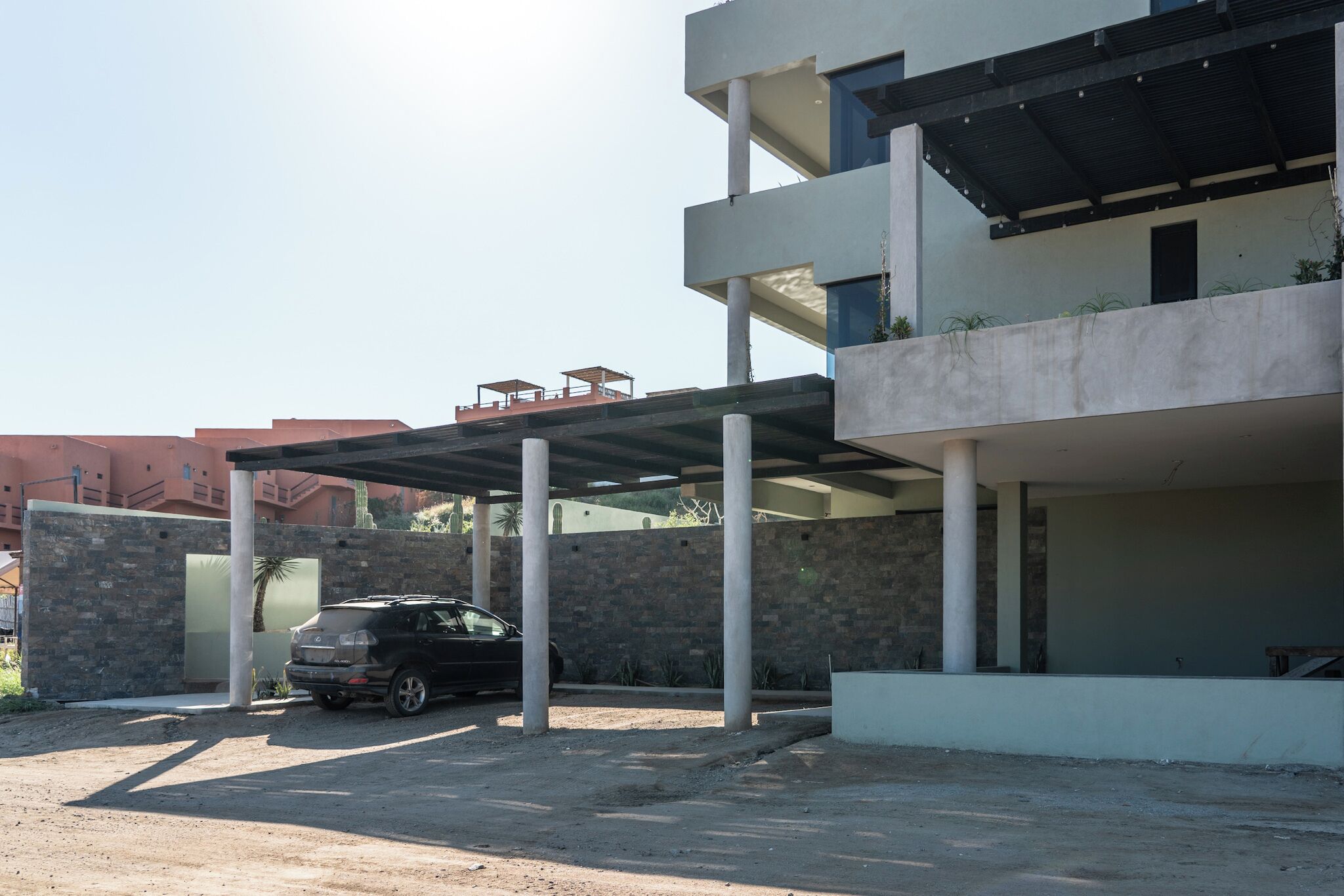 Un edifici modern amb zona de pàrquing coberta i un cotxe negre hi estacionat.