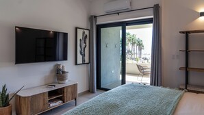 Un dormitorio moderno con una cama grande, un televisor de pantalla plana montado en la pared, una pequeña consola y un divisor corredizo que da a un espacio exterior con una silla y plantas.
