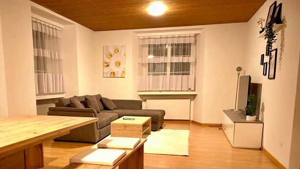 Un salon moderne avec un plancher en bois, un canapé, une table basse et une table à manger avec des bancs.