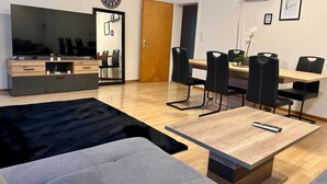 Un salon moderne comprenant un canapé, une table basse, un téléviseur, un coin repas avec des chaises et un meuble en bois.