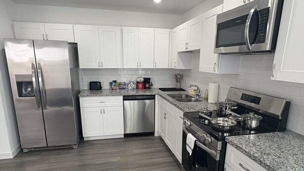 Una cocina moderna con armarios blancos, electrodomésticos de acero inoxidable, encimera de granito y suelo de madera.