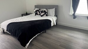 Un dormitorio con cama, mesita de noche y ventana con cortinas.