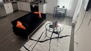 Un apartamento moderno con sala de estar que incluye un sofá negro, una mesa de centro de vidrio y un tapete estampado.