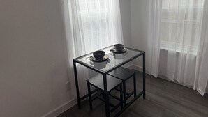 Una pequeña mesa de madera oscura con dos cuencos y una superficie de vidrio, ubicada en una esquina con cortinas blancas y translúcidas.
