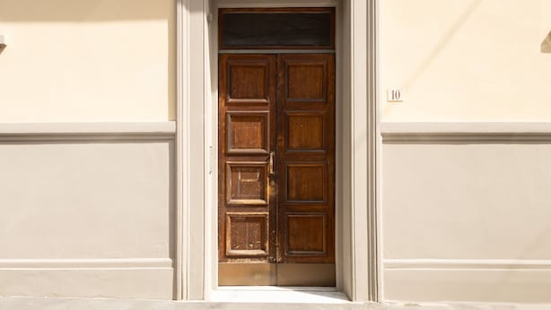 Una puerta de madera con manija de latón, enmarcada por un blanco, con el número '10' visible en la pared a la derecha.