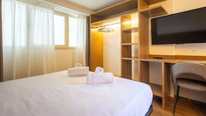 Una habitación de hotel con cama, televisión, una silla y una estantería de madera.
