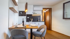 Una cocina moderna con gabinetes blancos, encimera negra y microondas integrado. Hay una mesa de comedor con dos sillas y una botella de vino.