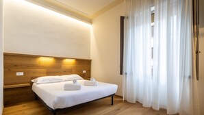 A hotel room with a wooden headboard, a bed with white linens, and a window with sheer curtains. - Cetra Suite a stone's throw from Santa Maria Novella (Firenze)