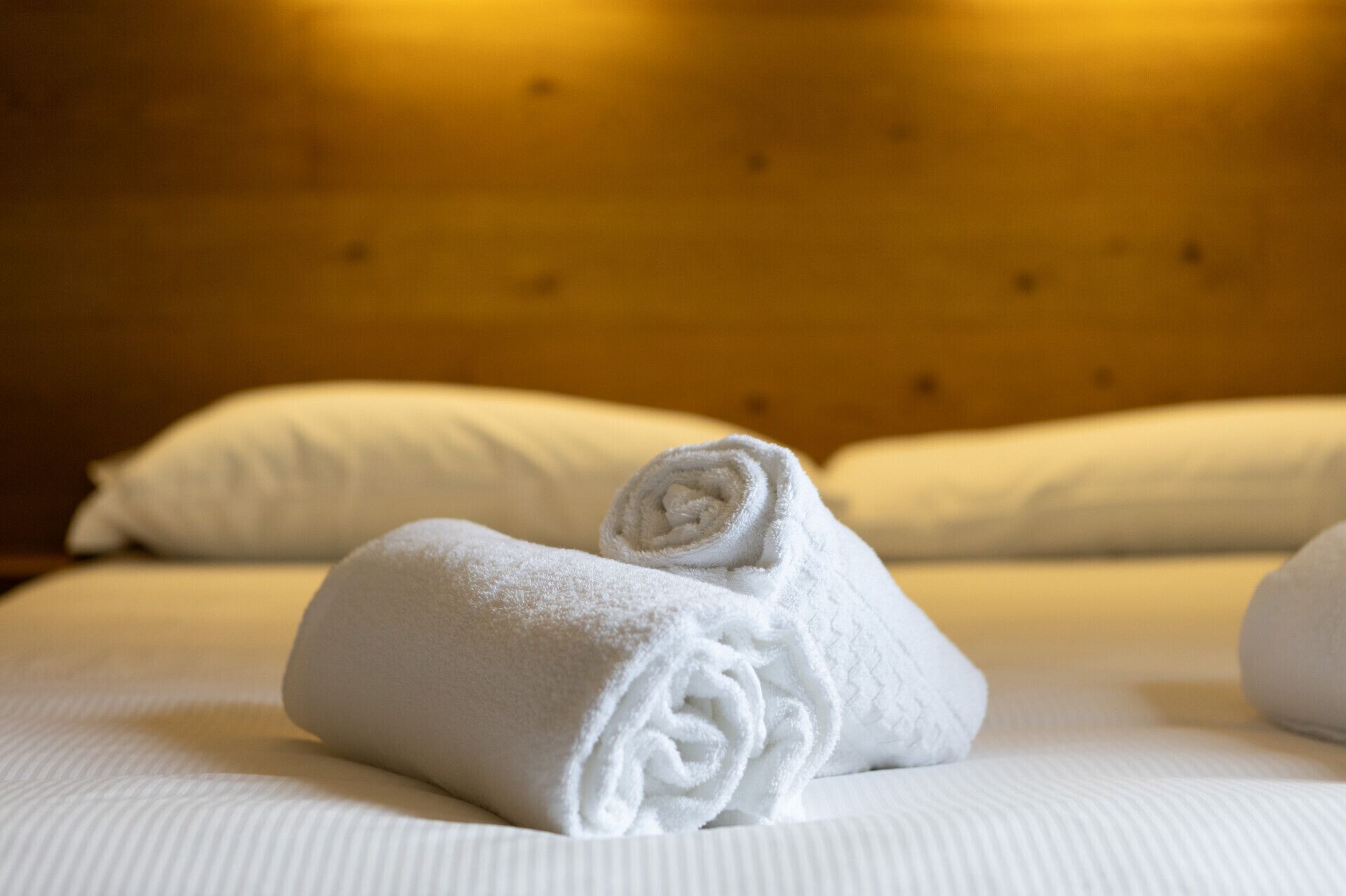 A neatly made bed with white linens and a rolled towel placed on it.