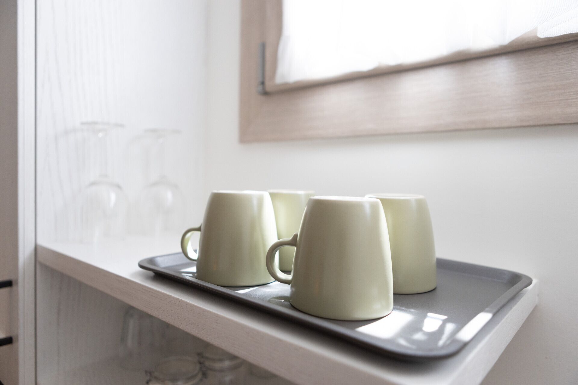A tray with three white mugs on a white countertop near a window.