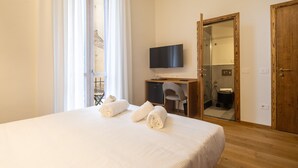 Hotellihuone, jossa on sänky, työpöytä, jossa on televisio, tuoli ja avoimesta ovesta näkyvä kylpyhuone.