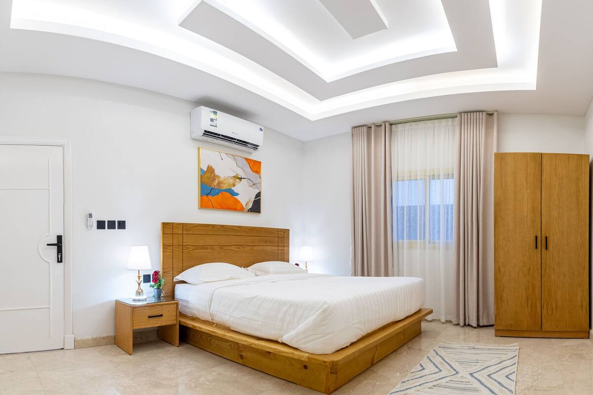 A modern bedroom with a wooden bed, a nightstand, a wardrobe, and a ceiling with recessed lighting.