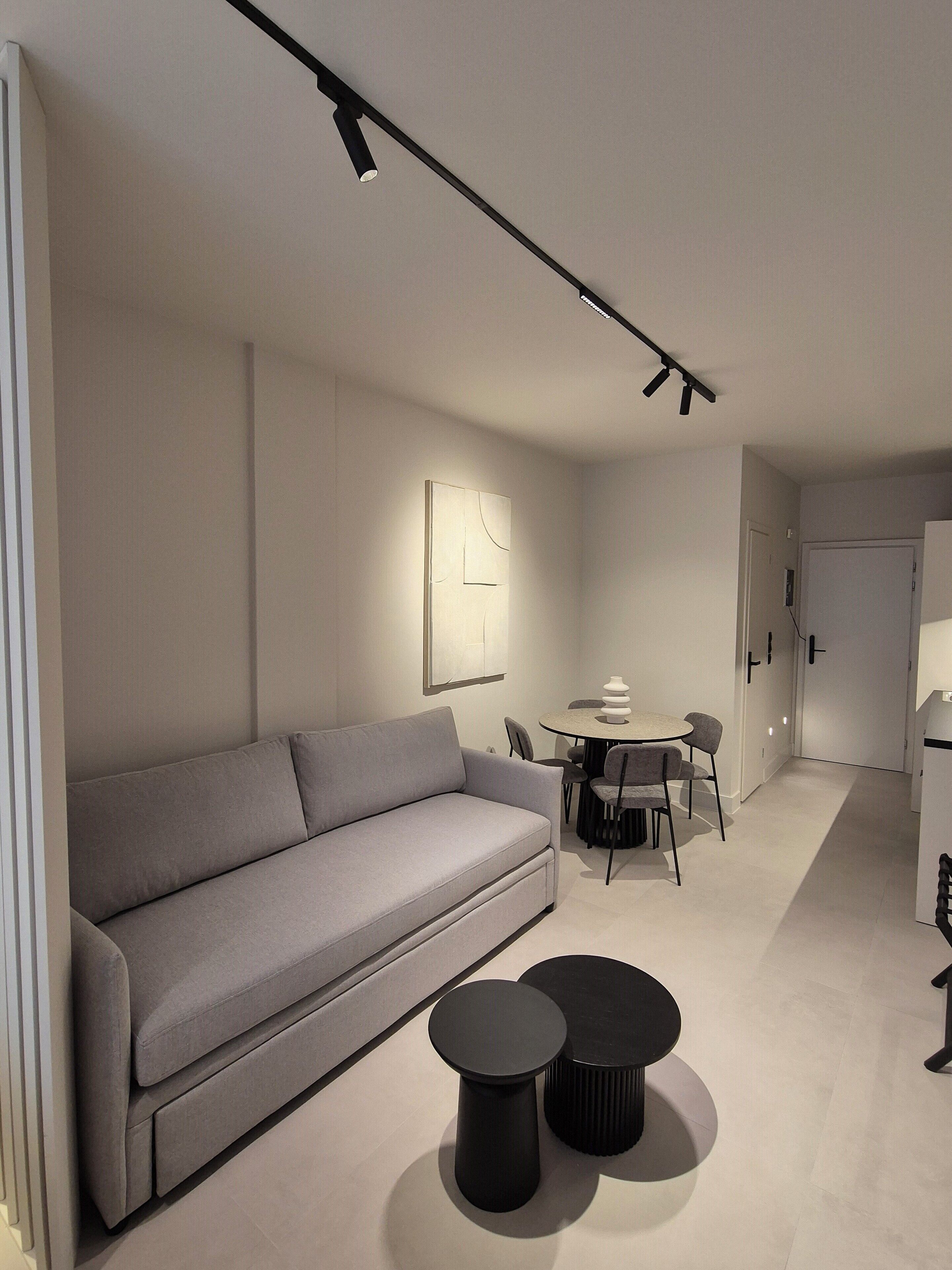 A modern living room with a grey sofa, a round dining table with chairs, and two black side tables.
