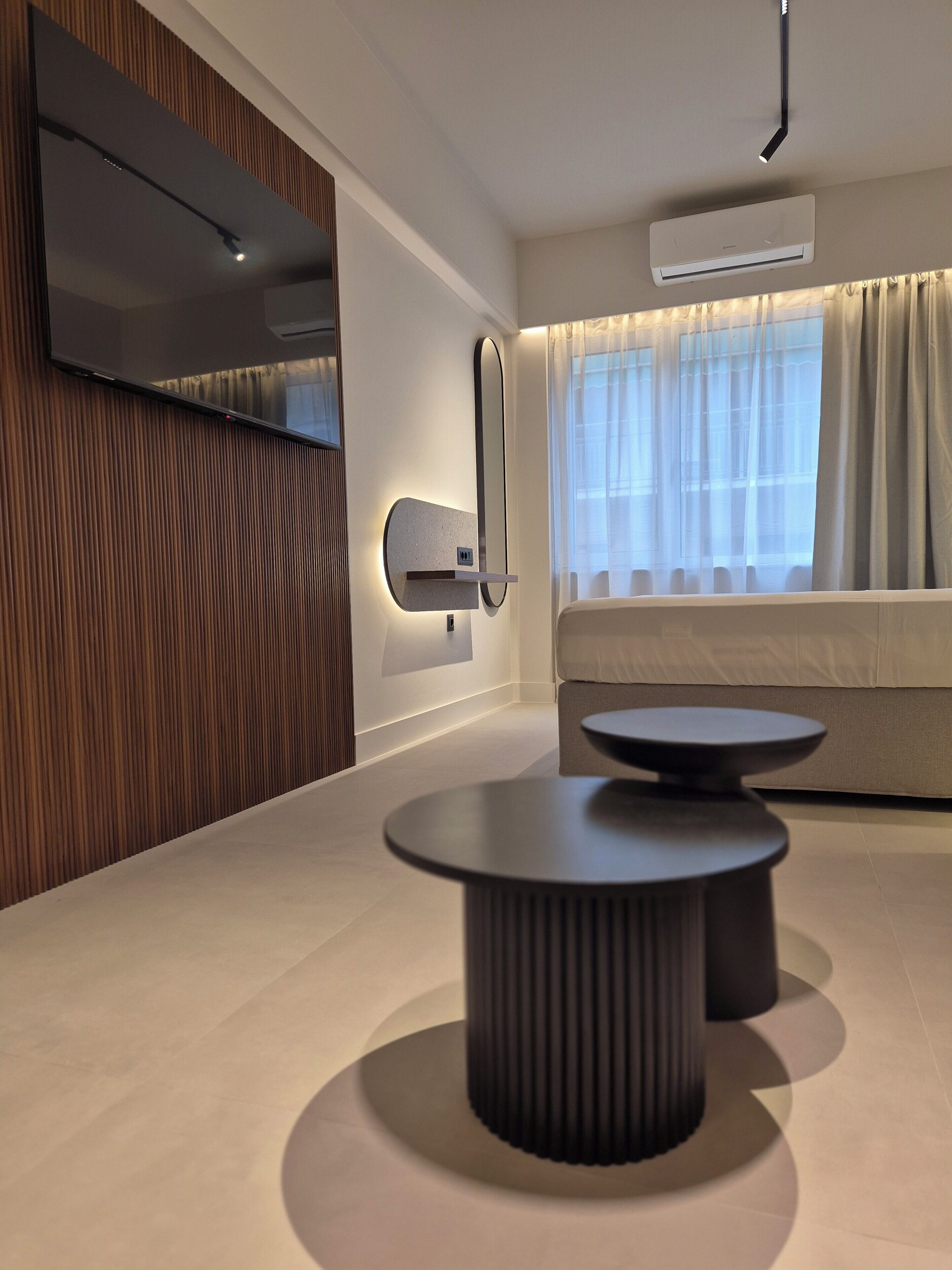 A modern living room with a flat-screen TV, a wall-mounted air conditioner, a sofa, and a round coffee table.