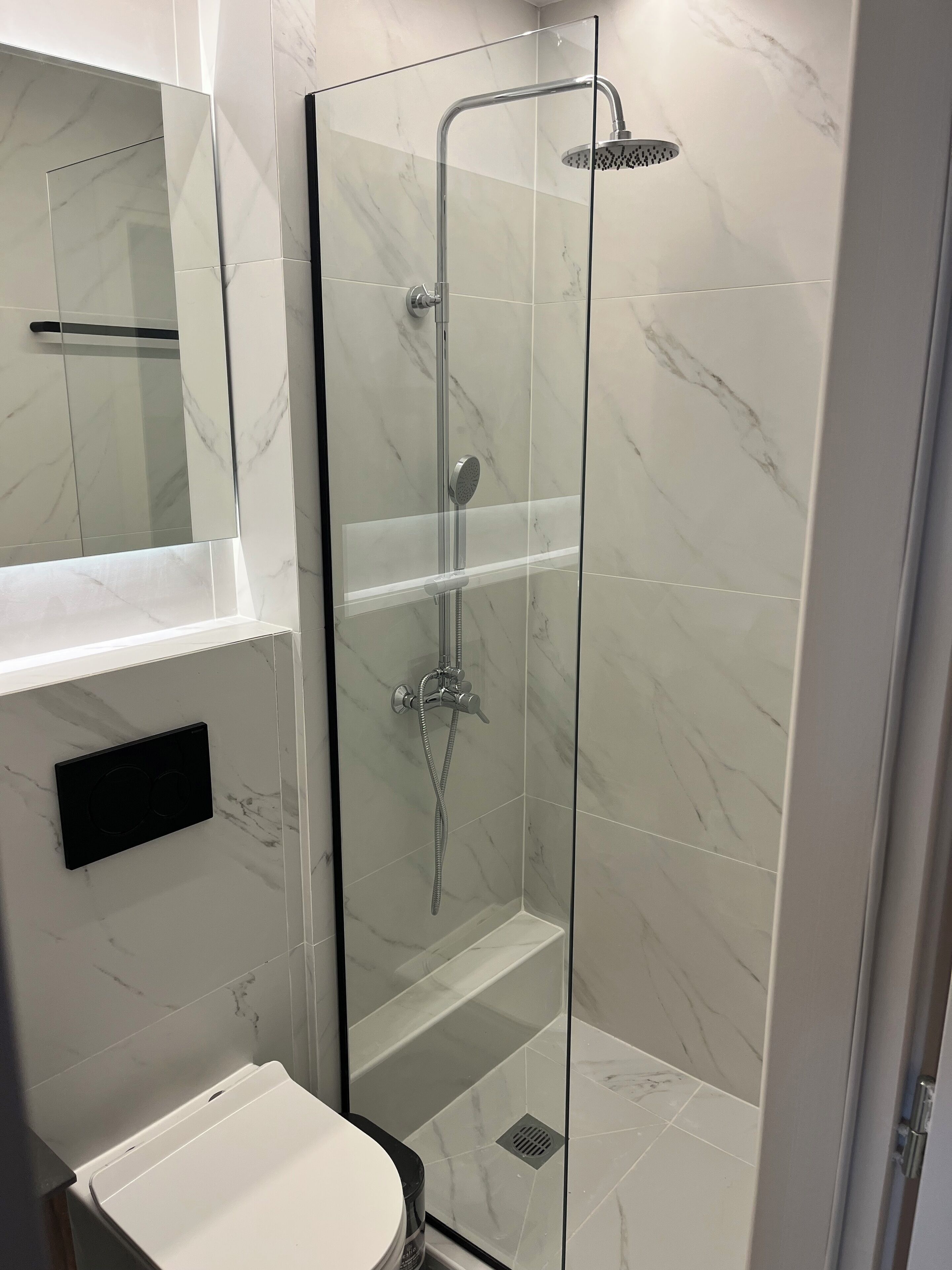 A modern bathroom with a glass-enclosed shower, a white sink, and a marble-tiled wall.