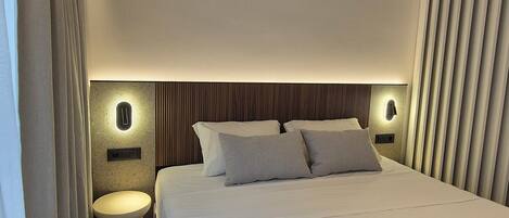 Quarto de hotel moderno com uma cama grande, mesas de cabeceira e painel de cabeceira embutido com iluminação integrada.
