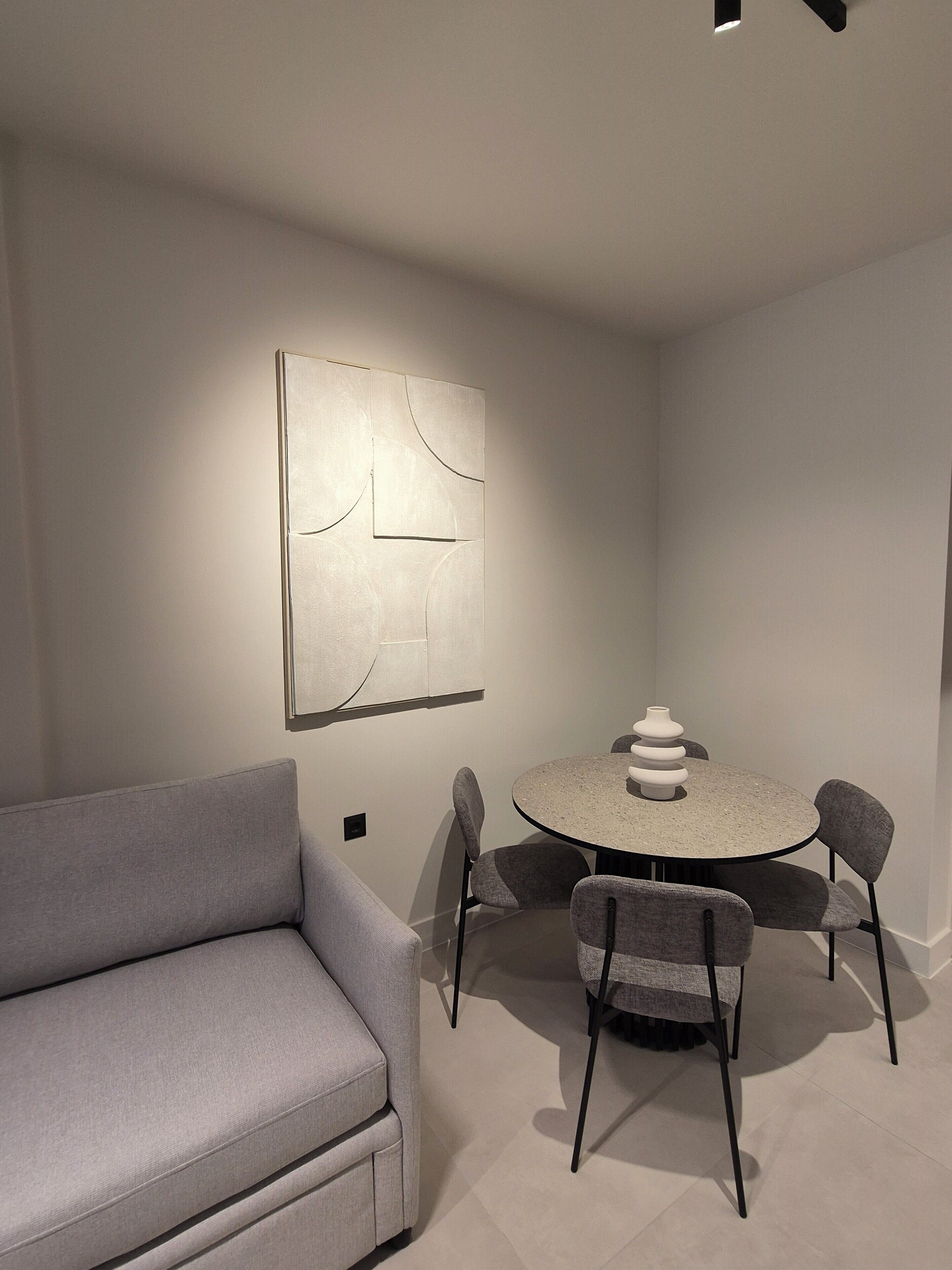 Een moderne eethoek met een ronde tafel, vier stoelen en een grijze bank.
