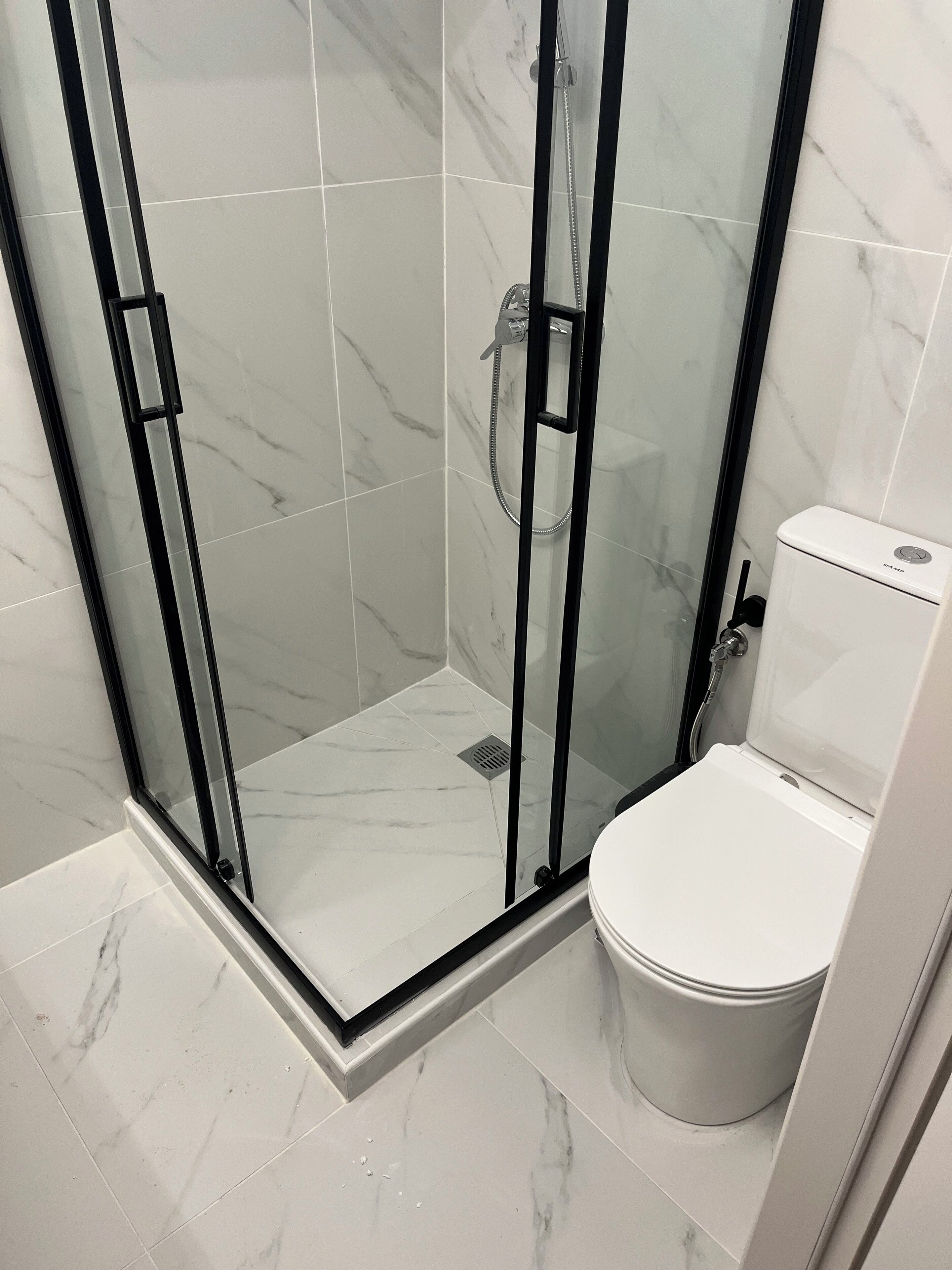 A bathroom with a glass-enclosed shower, a toilet, and a marble-tiled floor.