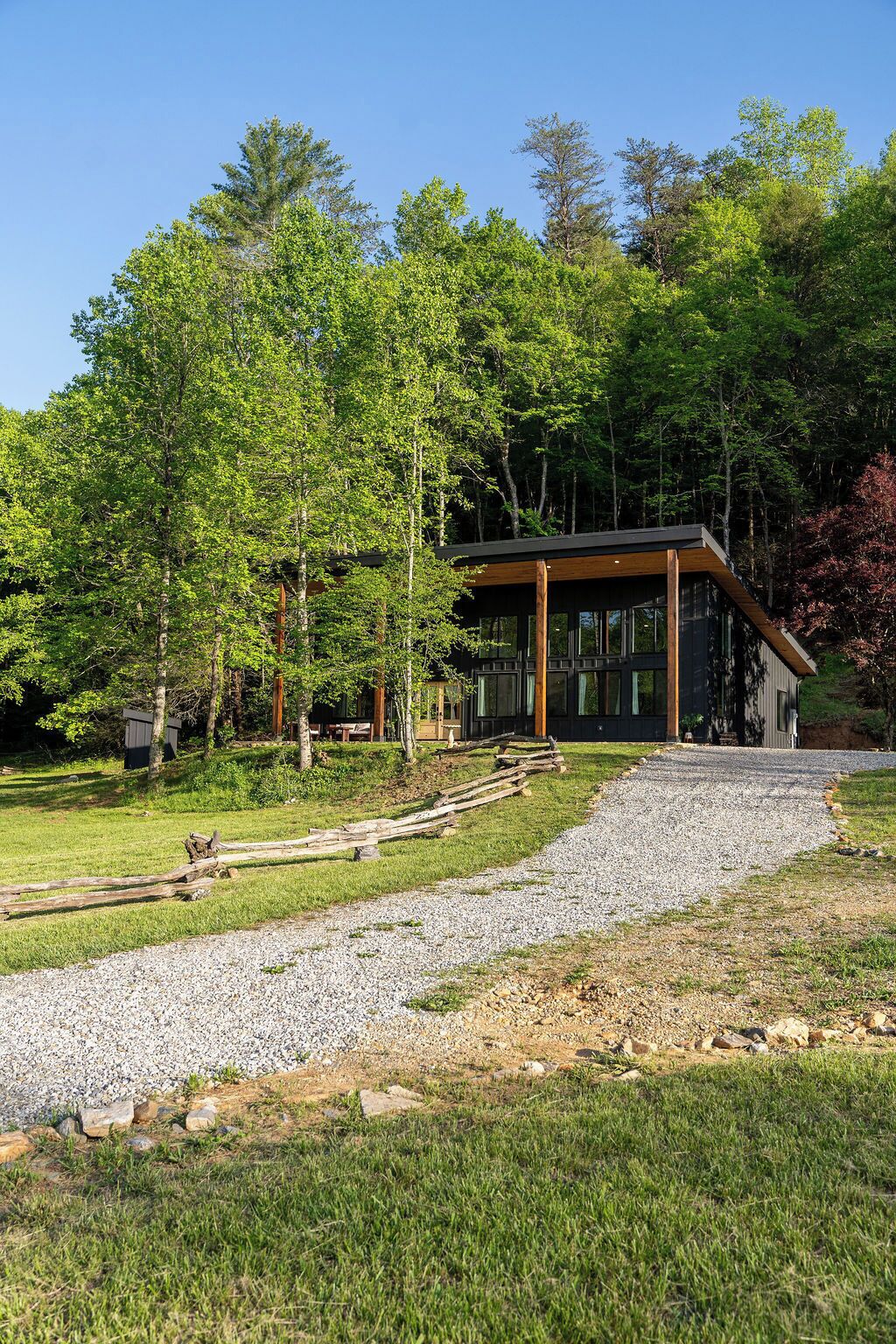 A modern building with a wooden deck, surrounded by trees and a gravel path.