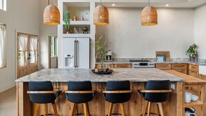 Una cocina moderna con una isla de mármol, taburetes negros y lámparas colgantes de mimbre.
