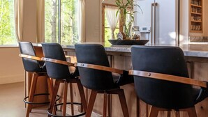 Cocina moderna con barra, con taburetes de madera, iluminación colgante y vistas al exterior.