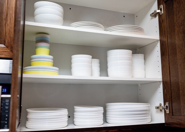 A cabinet with multiple shelves holding stacks of white plates and a colorful stack of plates on the left.