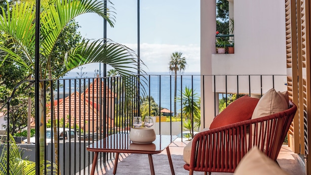 A balcony with a red chair, a small table, and a view of the ocean.