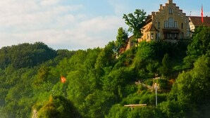 Un bâtiment historique à la façade en pierre, situé sur une falaise surplombant une rivière aux eaux tumultueuses.