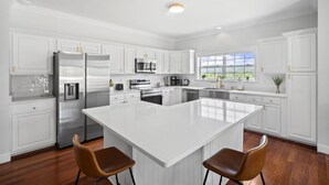 Una cocina moderna con armarios blancos, electrodomésticos de acero inoxidable y una isla grande con dos taburetes de bar.