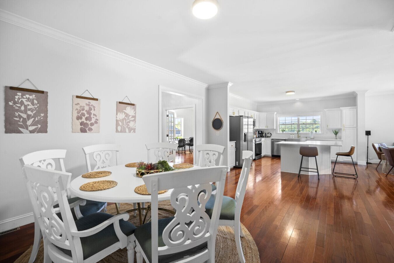 A spacious kitchen with white cabinets, a central island, and a dining area with white chairs and a round table.