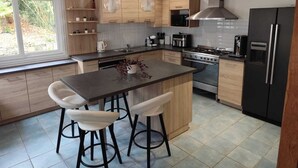 A modern kitchen with a central island, bar stools, stainless steel appliances, and pendant lighting. - Charming family home (Taulé)