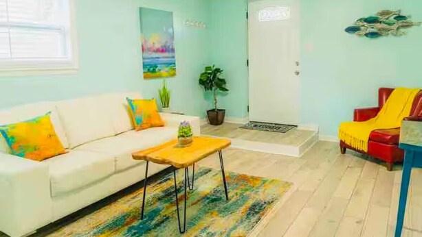 Un salon avec un canapé blanc, une petite table en bois, un tapis coloré, une plante en pot et un fauteuil rouge.