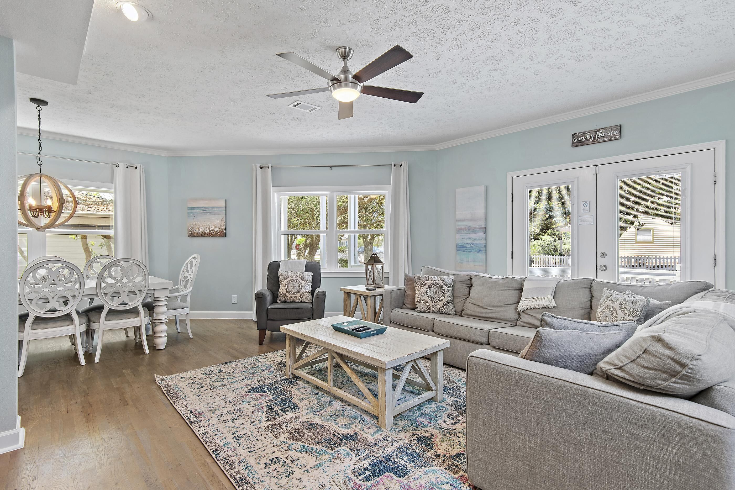 A spacious living room with a ceiling fan, a dining area with white chairs, a gray sofa, and a patterned rug.