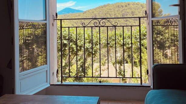 Una habitación con un ventanal amplio, barandilla metálica de balcón, una mesa con una revista y un sofá verde.