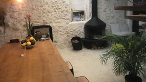 Un interior rústico con una pared de piedra, una mesa de madera con frutas, una chimenea y una escalera.
