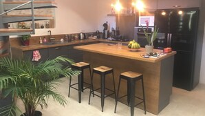 Una cocina moderna con una isla central, taburetes de bar, una escalera de caracol y un refrigerador.