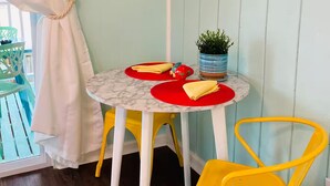 Una habitación con una mesa redonda, dos sillas amarillas, una cama blanca y un cuadro en la pared.