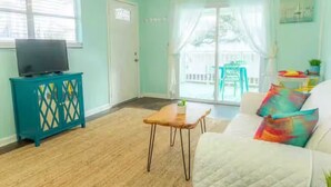 Una sala de estar con paredes color turquesa, un sofá blanco, una mesa de centro de madera y un televisor sobre un mueble turquesa.