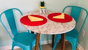 Een kleine ronde tafel met twee stoelen, elk met een rode tafelmat en een gele servet.
