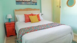 Een slaapkamer met een bed, nachtkastje, schilderij en een deur.