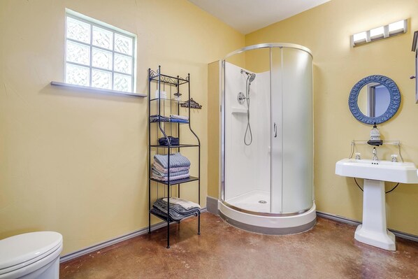 A bathroom with a glass-enclosed shower, a white sink with a mirror, and a towel rack with folded towels.