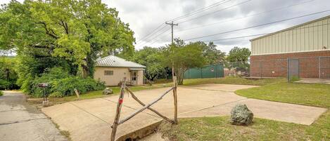 A residential area with a paved driveway, a mailbox, a wooden gate, a large rock, and a brick building in the background.
