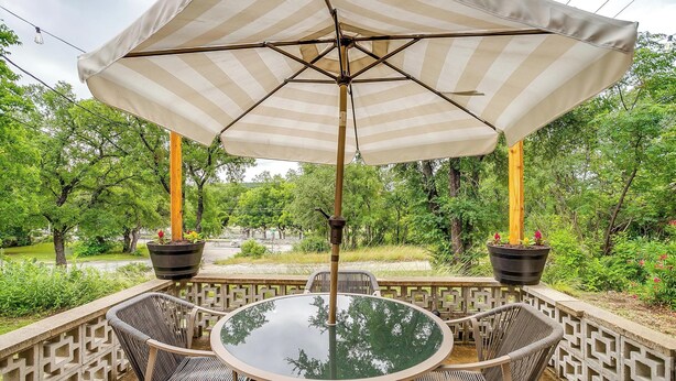 A round glass table with wicker chairs and a striped canopy umbrella. - Villa 101 · Peaceful River Views · Steps to Water (Glen Rose)